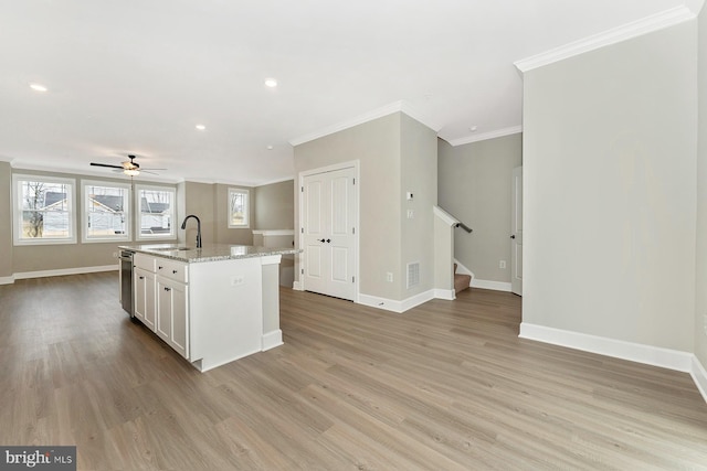 kitchen with white cabinets, open floor plan, light stone countertops, a kitchen island with sink, and a sink