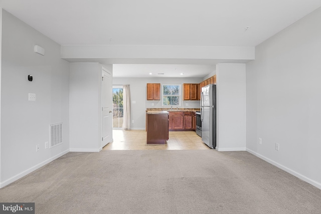 kitchen featuring light colored carpet, stainless steel appliances, open floor plan, light countertops, and brown cabinetry