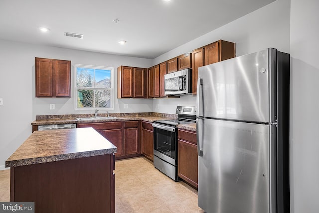 kitchen featuring visible vents, dark countertops, appliances with stainless steel finishes, a center island, and a sink