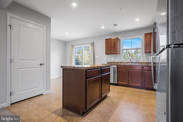 kitchen with visible vents, dark countertops, a kitchen island, stainless steel appliances, and a sink