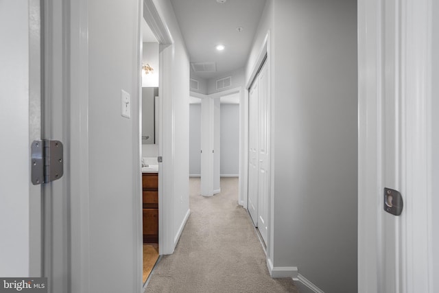 hallway with baseboards, visible vents, and light colored carpet