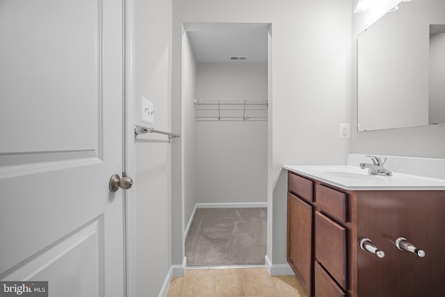 bathroom with a walk in closet, visible vents, vanity, and baseboards