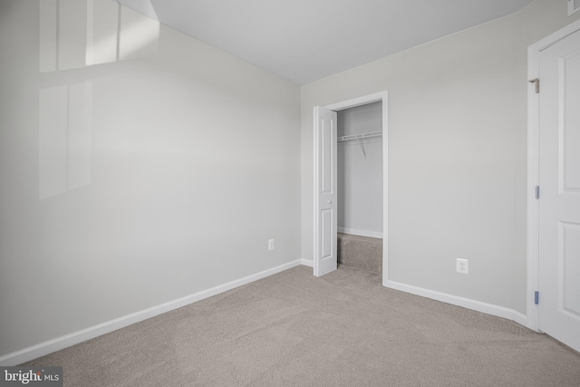 unfurnished bedroom with a closet, light colored carpet, a spacious closet, and baseboards