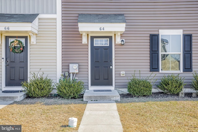 view of exterior entry with roof with shingles and a yard