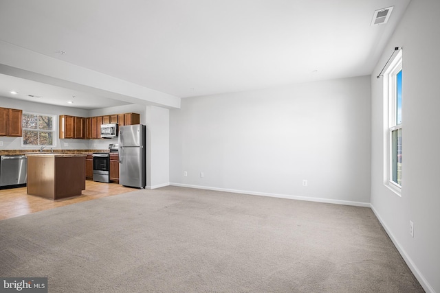 kitchen with open floor plan, appliances with stainless steel finishes, light colored carpet, and a center island