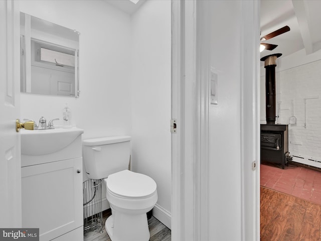 bathroom with toilet, a wood stove, vanity, wood finished floors, and baseboards