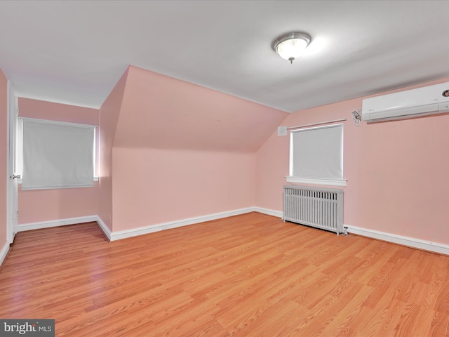 additional living space featuring lofted ceiling, light wood-type flooring, radiator, and an AC wall unit