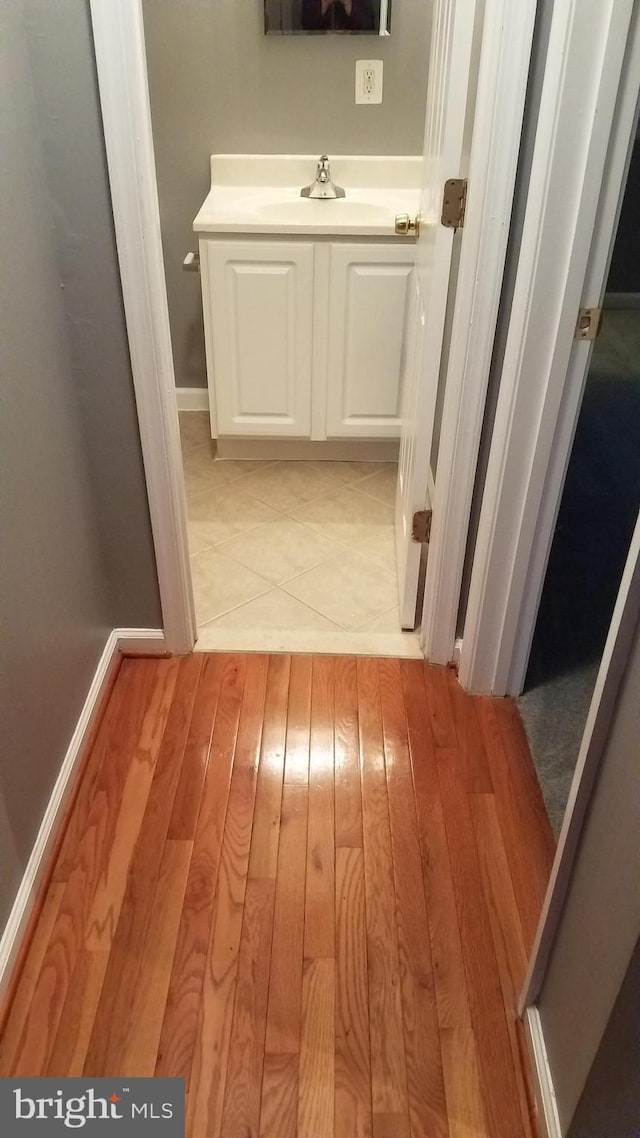 hallway featuring baseboards, a sink, and light wood-style floors