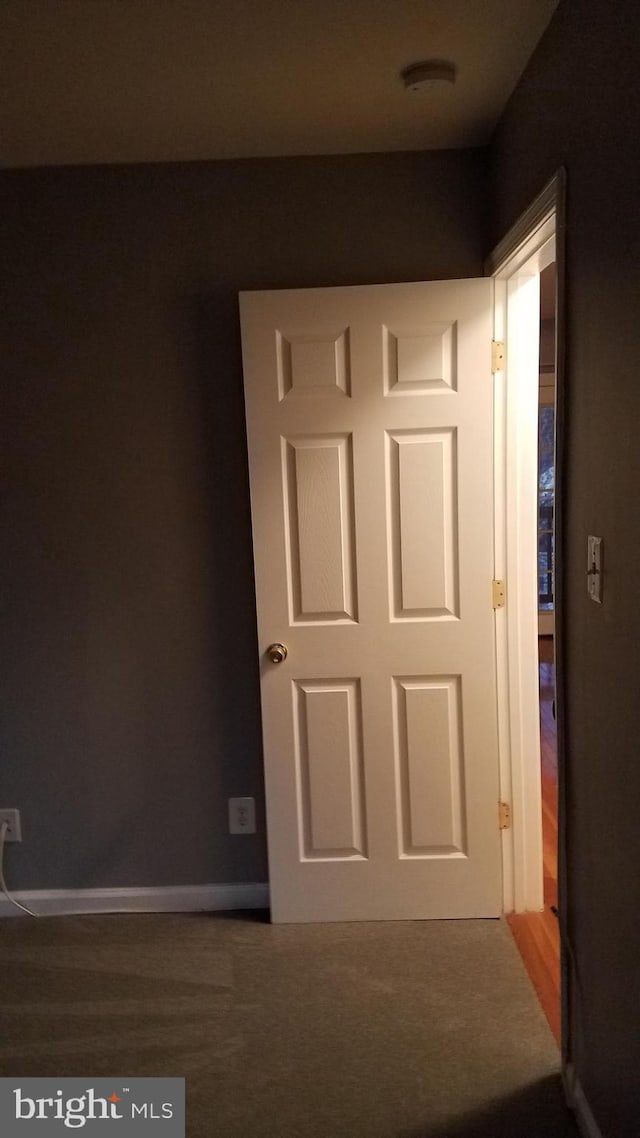 hallway with baseboards and dark carpet