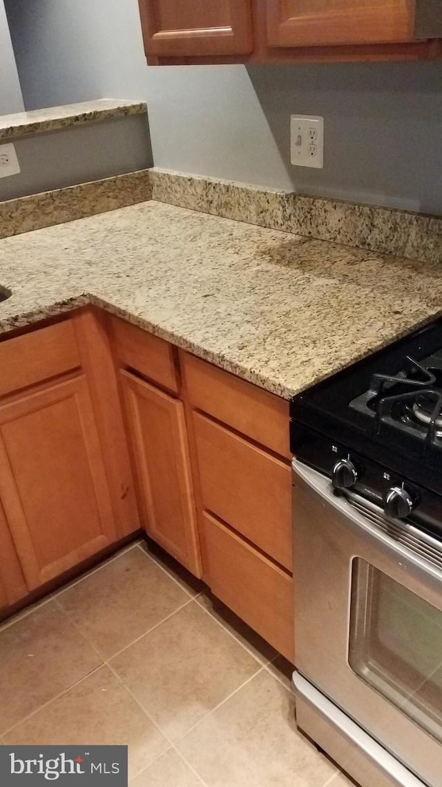 kitchen featuring brown cabinetry, stainless steel range with gas cooktop, light stone counters, and light tile patterned floors