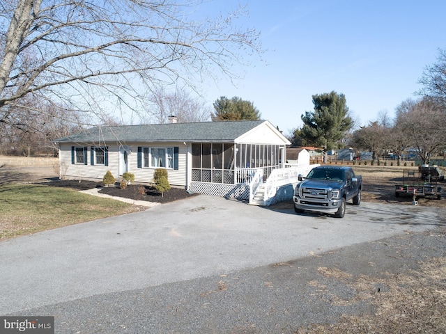 view of front of house with aphalt driveway, a chimney, a shingled roof, and a sunroom