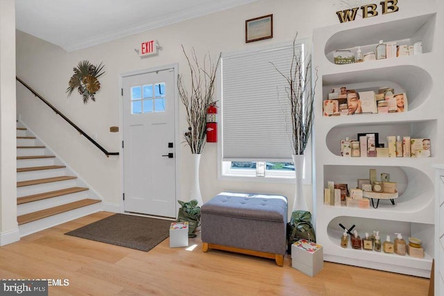 entryway featuring a wealth of natural light, stairway, crown molding, and wood finished floors