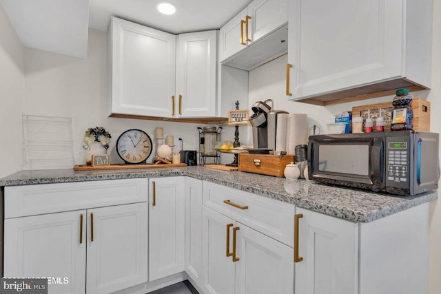 kitchen with black microwave, white cabinetry, and light stone countertops