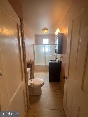 bathroom with radiator, toilet, tile patterned flooring, an enclosed shower, and vanity