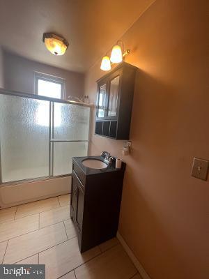 full bath featuring combined bath / shower with glass door, vanity, and tile patterned floors