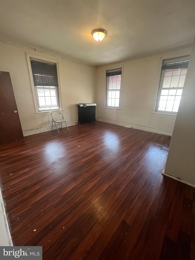 unfurnished room featuring dark wood-type flooring, ornamental molding, and baseboards