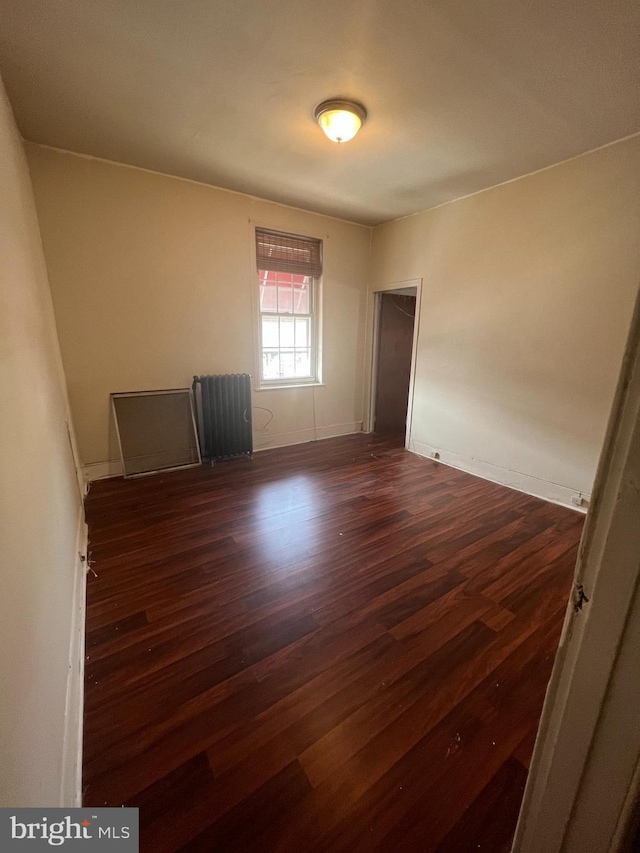 empty room featuring baseboards, dark wood finished floors, and radiator