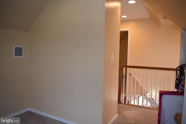 hallway featuring carpet, visible vents, vaulted ceiling, and an upstairs landing