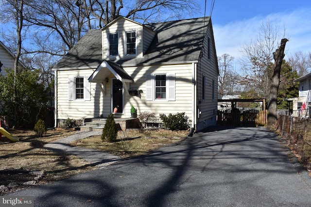 cape cod home with aphalt driveway, fence, and a shingled roof