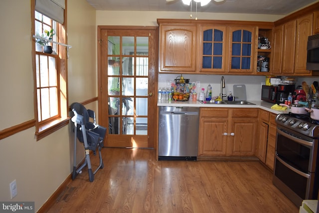 kitchen featuring light countertops, light wood-style flooring, appliances with stainless steel finishes, brown cabinetry, and a sink