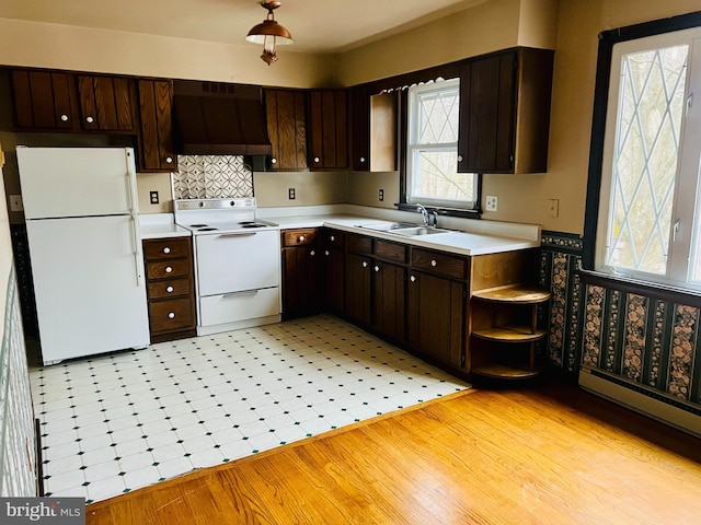 kitchen featuring dark brown cabinetry, white appliances, wall chimney exhaust hood, light countertops, and a sink