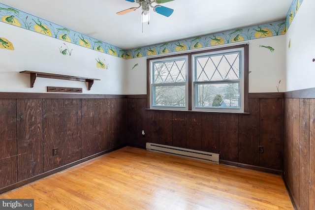 empty room featuring a baseboard heating unit, wood finished floors, and wainscoting