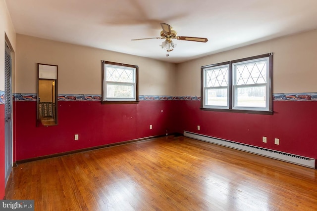 spare room featuring a baseboard heating unit, ceiling fan, and wood finished floors