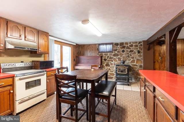 kitchen featuring black microwave, wooden walls, under cabinet range hood, white electric range, and brown cabinets