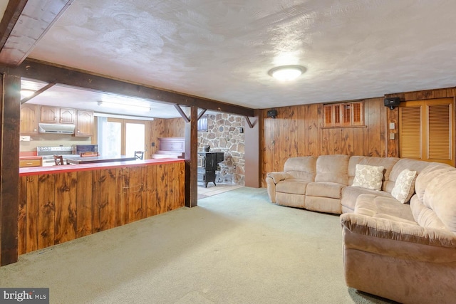 living area featuring a textured ceiling, beamed ceiling, wood walls, and light colored carpet