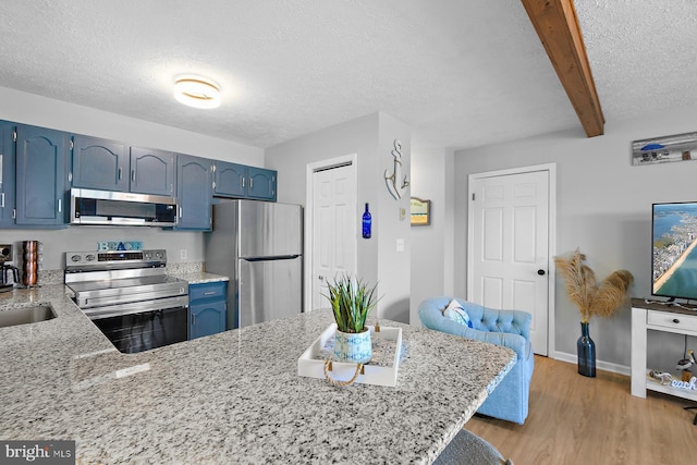 kitchen with blue cabinets, stainless steel appliances, a peninsula, beam ceiling, and light wood finished floors