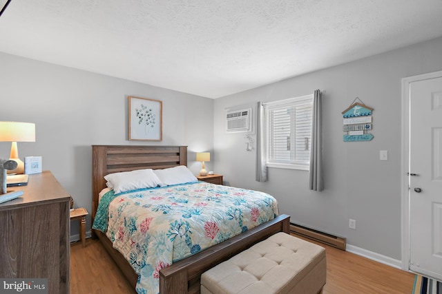 bedroom with a textured ceiling, wood finished floors, baseboards, baseboard heating, and a wall mounted AC