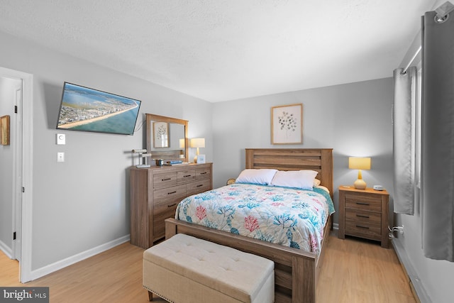 bedroom with light wood-style flooring, baseboards, and a textured ceiling