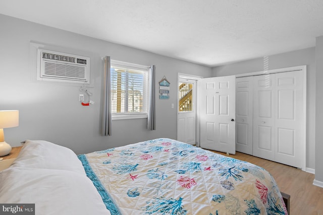 bedroom featuring light wood-style floors, a closet, a wall mounted air conditioner, and a textured ceiling