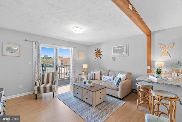 living room with a textured ceiling, baseboards, light wood-style floors, an AC wall unit, and beamed ceiling