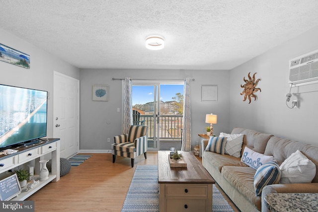 living area featuring a wall mounted AC, light wood-style flooring, baseboards, and a textured ceiling