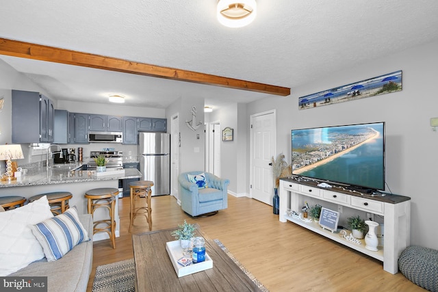 living room featuring light wood-style floors, beam ceiling, a textured ceiling, and baseboards