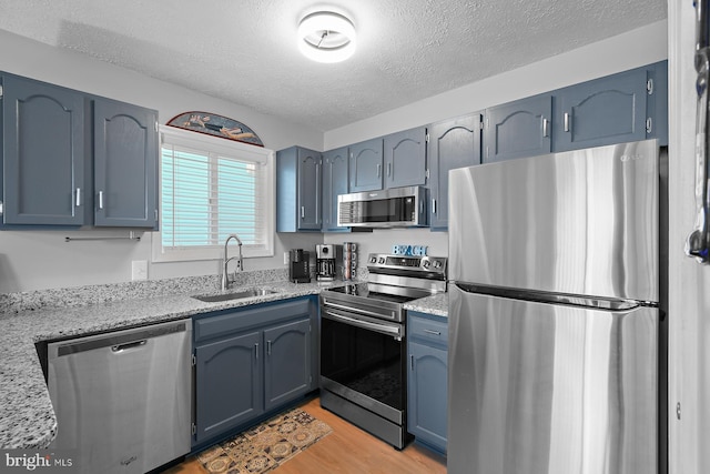 kitchen with a textured ceiling, light stone counters, light wood-style flooring, stainless steel appliances, and a sink