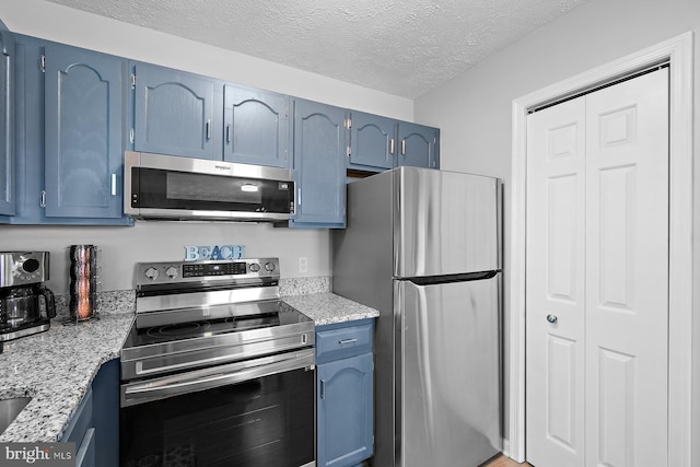 kitchen with stainless steel appliances, a textured ceiling, blue cabinetry, and light stone countertops