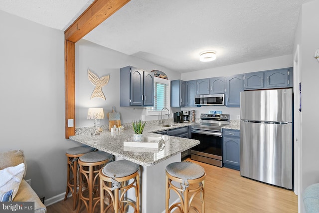 kitchen featuring appliances with stainless steel finishes, light wood-style floors, a peninsula, and light stone counters