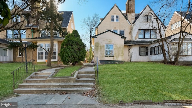 english style home featuring a chimney, a front yard, and stucco siding