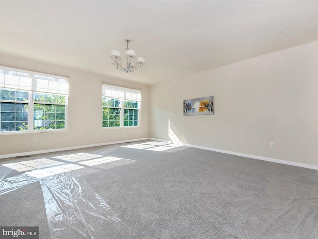 spare room featuring carpet flooring, a notable chandelier, visible vents, and baseboards