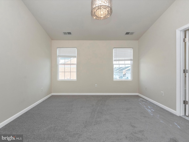 spare room featuring a chandelier, carpet, visible vents, and baseboards