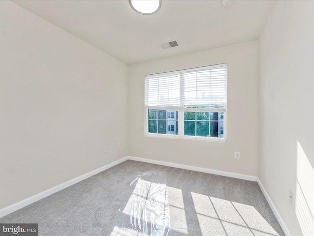 spare room featuring light colored carpet, visible vents, and baseboards