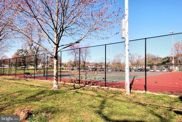 view of tennis court featuring a lawn and fence