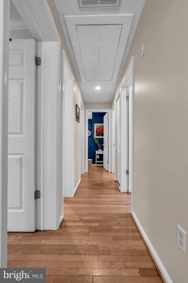 hall with attic access, light wood-type flooring, and baseboards