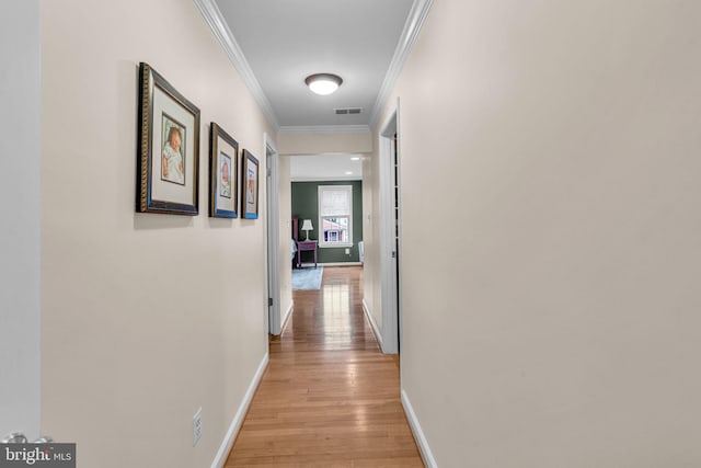 hall featuring visible vents, ornamental molding, light wood-style flooring, and baseboards