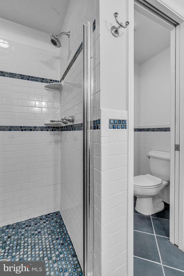 bathroom featuring toilet, a stall shower, and tile walls