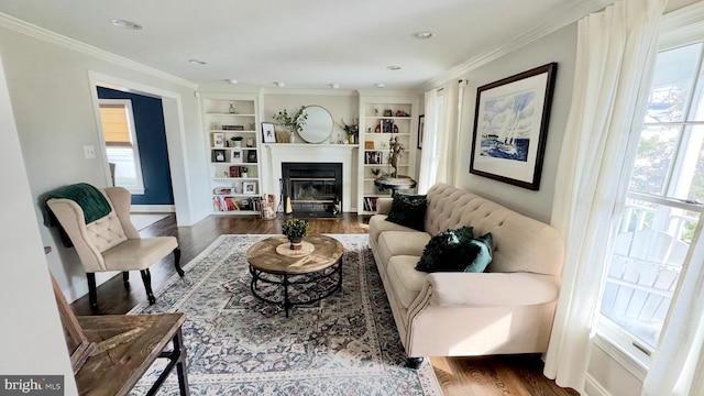 living area featuring a fireplace with flush hearth, built in shelves, ornamental molding, and wood finished floors