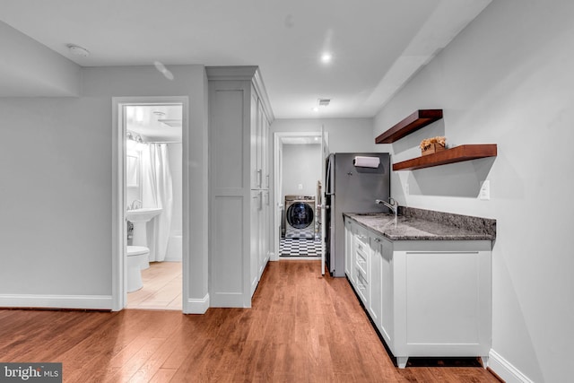 kitchen with open shelves, washer / clothes dryer, light wood-style floors, dark stone counters, and baseboards