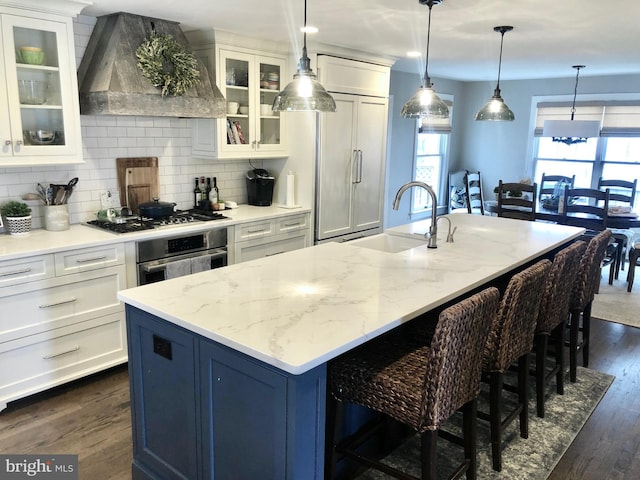 kitchen featuring dark wood finished floors, custom range hood, stainless steel appliances, a kitchen bar, and a sink